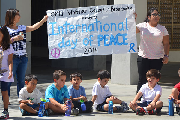 OMEP members hold up an International Day of Peace sign with students.