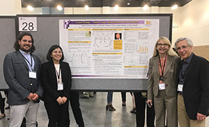 Two students and two professors stand in front of a poster presentation.