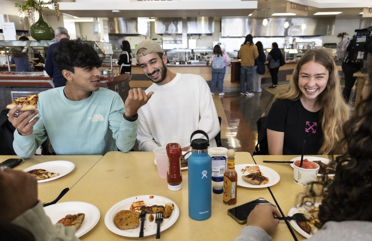 Two male students sitting next to female student laughing in cafeteria