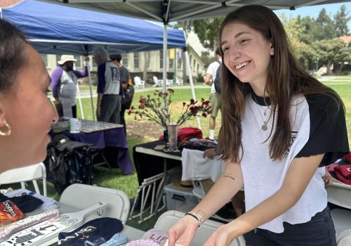 Female Whittier student handing promotional materials to fellow female student advertising their organization on campus