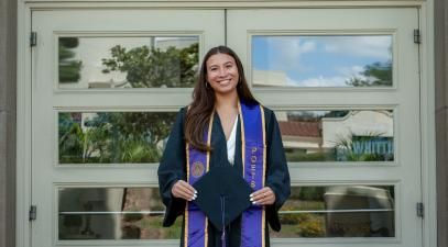 marin in grad regalia in front of Mendenhall