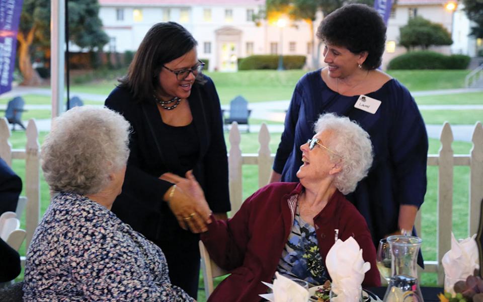 Linda Oubre between two female alumni, shaking hands with a third alumna.